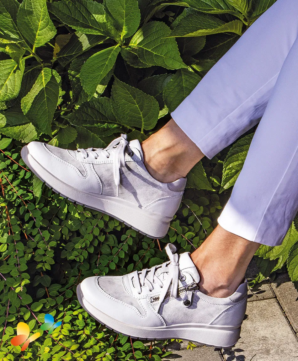 Eine Person trägt weiße Sneakers. Die Sonne scheint und die Umgebung ist grün.